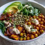 A vibrant vegetarian dinner bowl featuring roasted sweet potatoes, crispy chickpeas, garlicky spinach, and smoky tahini dressing.