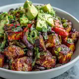 A colorful Sweet Potato and Black Bean Bowl features warm roasted vegetables, juicy cherry tomatoes, and a zesty lime dressing drizzled over crisp mixed greens.