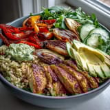 A close-up shows creamy avocado slices and crisp lemon salad garnishing the hearty Paprika Roasted Vegetable Quinoa Bowl.