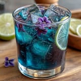 A mesmerizing glass of butterfly pea flower lemonade, shifting from deep blue to vibrant purple as citrus is added, served over ice with lemon slices.