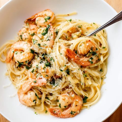 A close-up of Creamy Garlic Shrimp Pasta highlights glistening sauce, fresh parsley, and lemon wedges on a rustic table.