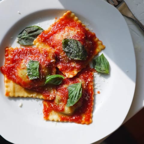 Homemade spinach ricotta ravioli with vibrant marinara sauce, fresh basil, and grated Parmesan for a cozy Italian dinner.