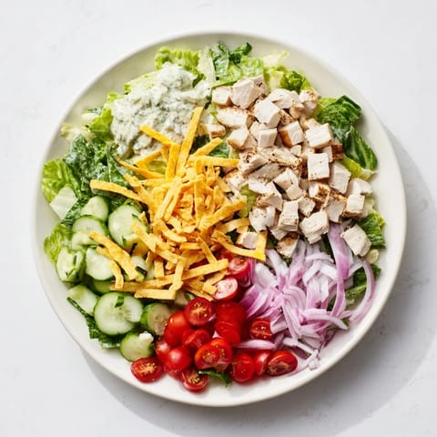 A hearty, chilled salad with tender chicken, diced cucumber, red onion, and cheddar cheese, drizzled with spicy ranch for a refreshing, satisfying meal.