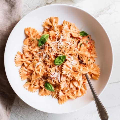 Fork twirling al dente farfalle coated in a silky tomato sauce, with vibrant green basil and a sprinkle of grated Parmesan cheese.