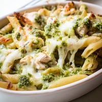 A golden-baked Pesto Chicken Pasta Bake with melted mozzarella, vibrant green basil pesto, and tender chicken in a ceramic dish.