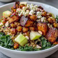 Vibrant Fall Harvest Bowl with roasted sweet potatoes, Brussels sprouts, and crispy chickpeas topped with almonds and feta.